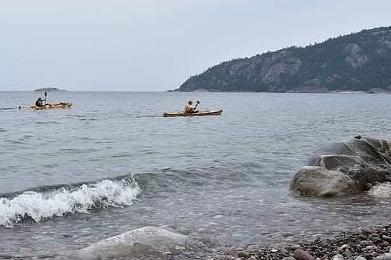 two kayakers paddling near shore on an overcast day